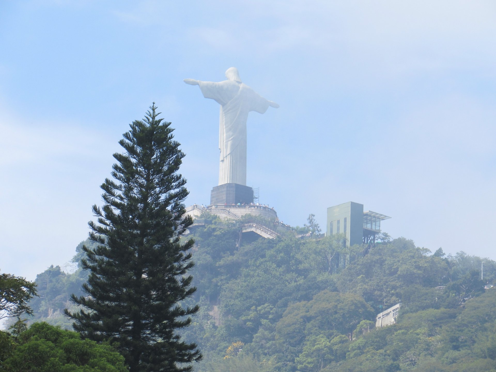 Cristo Redentor visto de longe no alto do morro, com o elevador panorâmico ao lado
