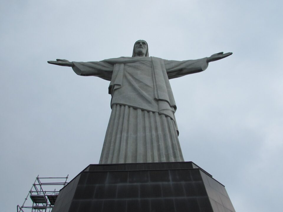 Cristo Redentor visto de baixo, com os braços abertos e a base de granito, em céu nublado