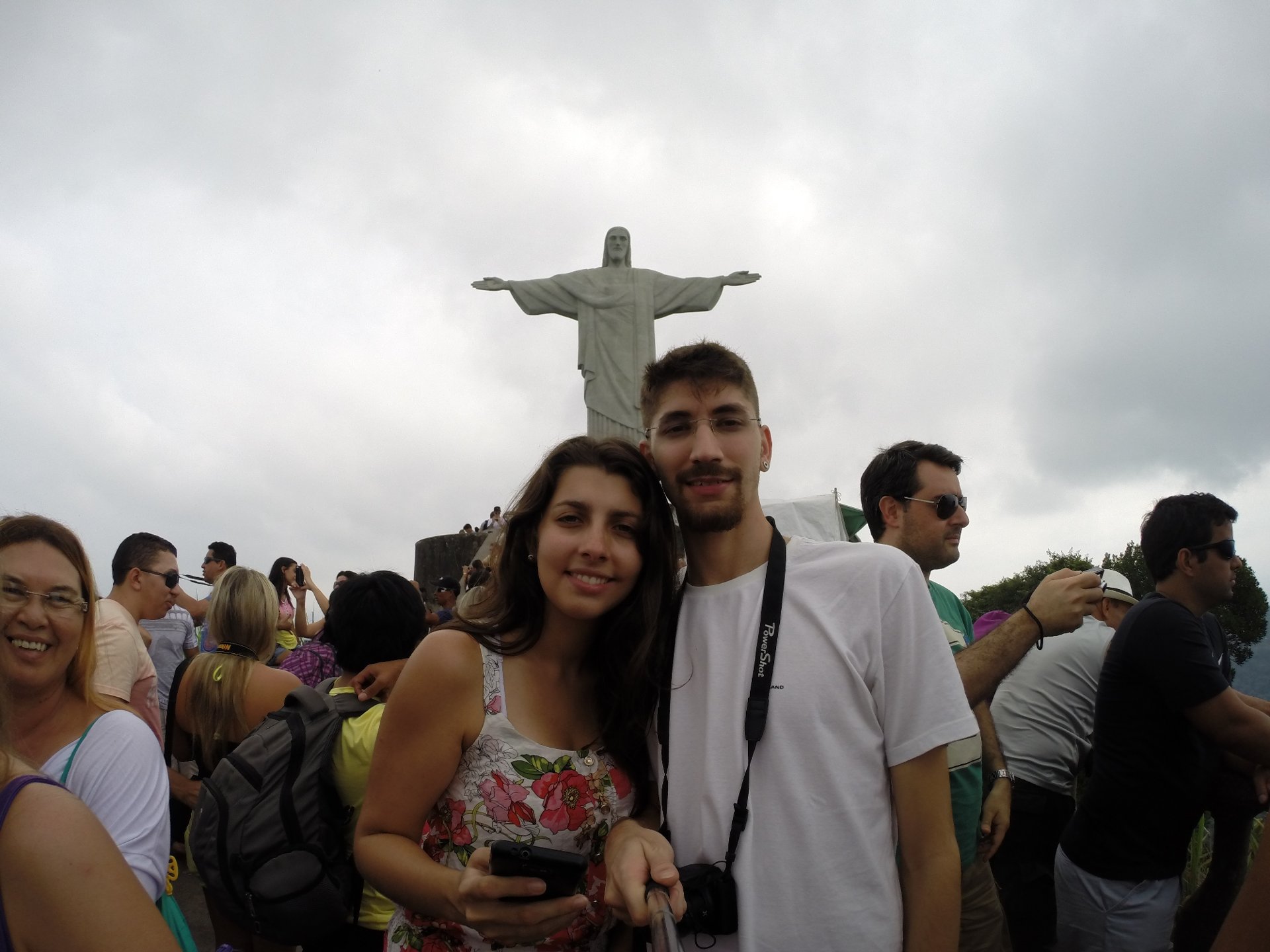 Casal tirando selfie com o Cristo Redentor ao fundo e muita gente na plataforma