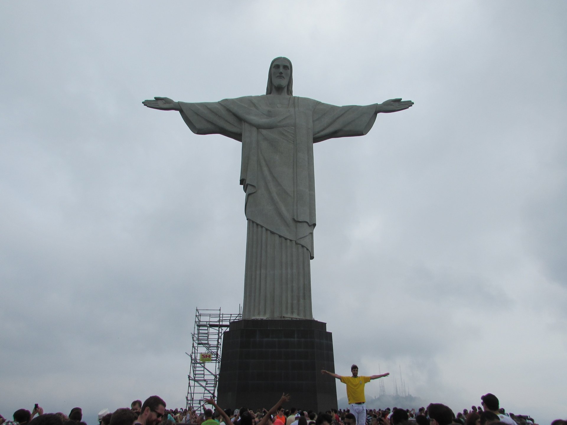 Pessoa de braços abertos na base do Cristo Redentor, que mostra a escala da estátua
