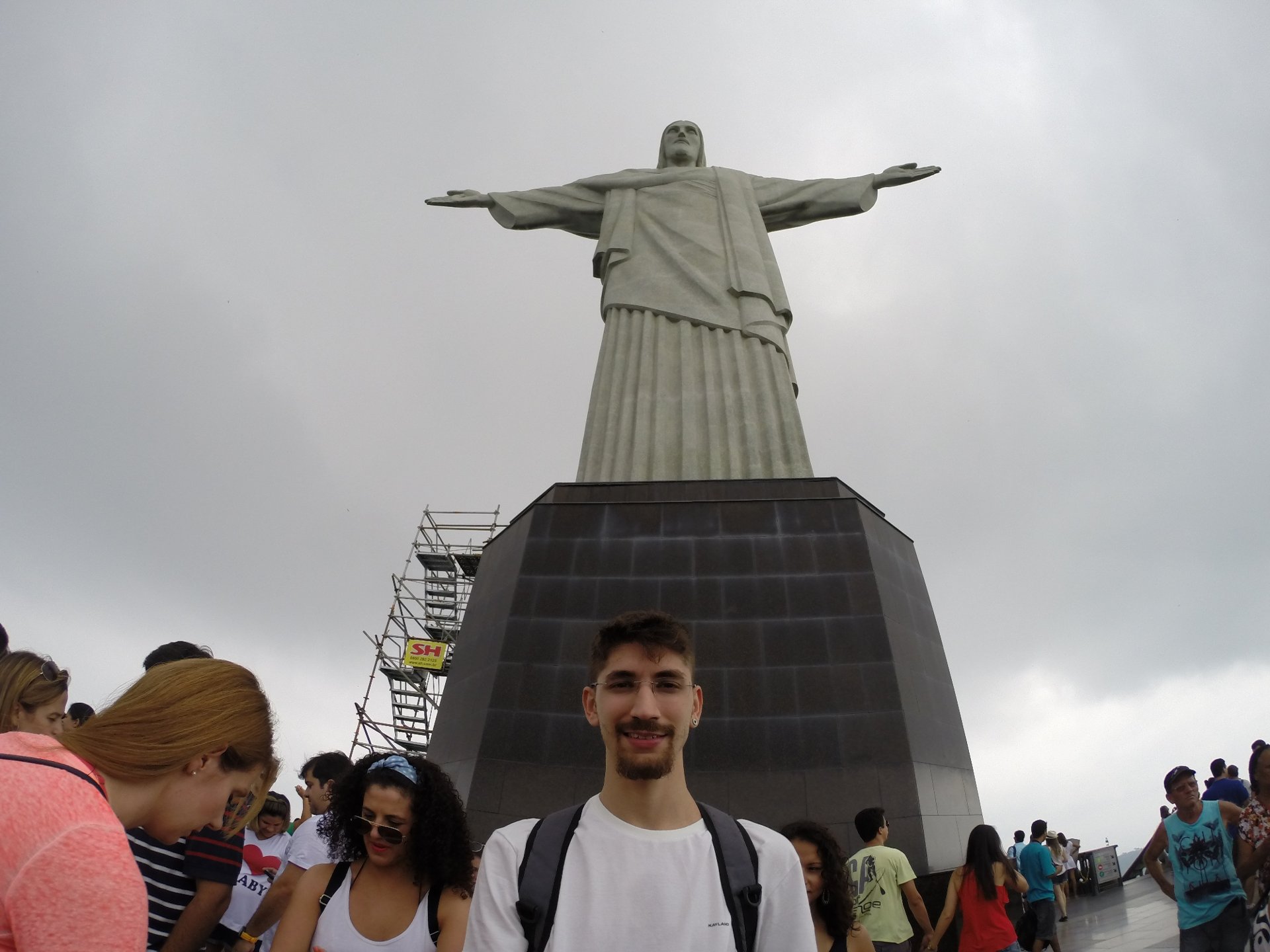 Visitante na base do Cristo Redentor, com a estátua ao fundo e turistas ao redor